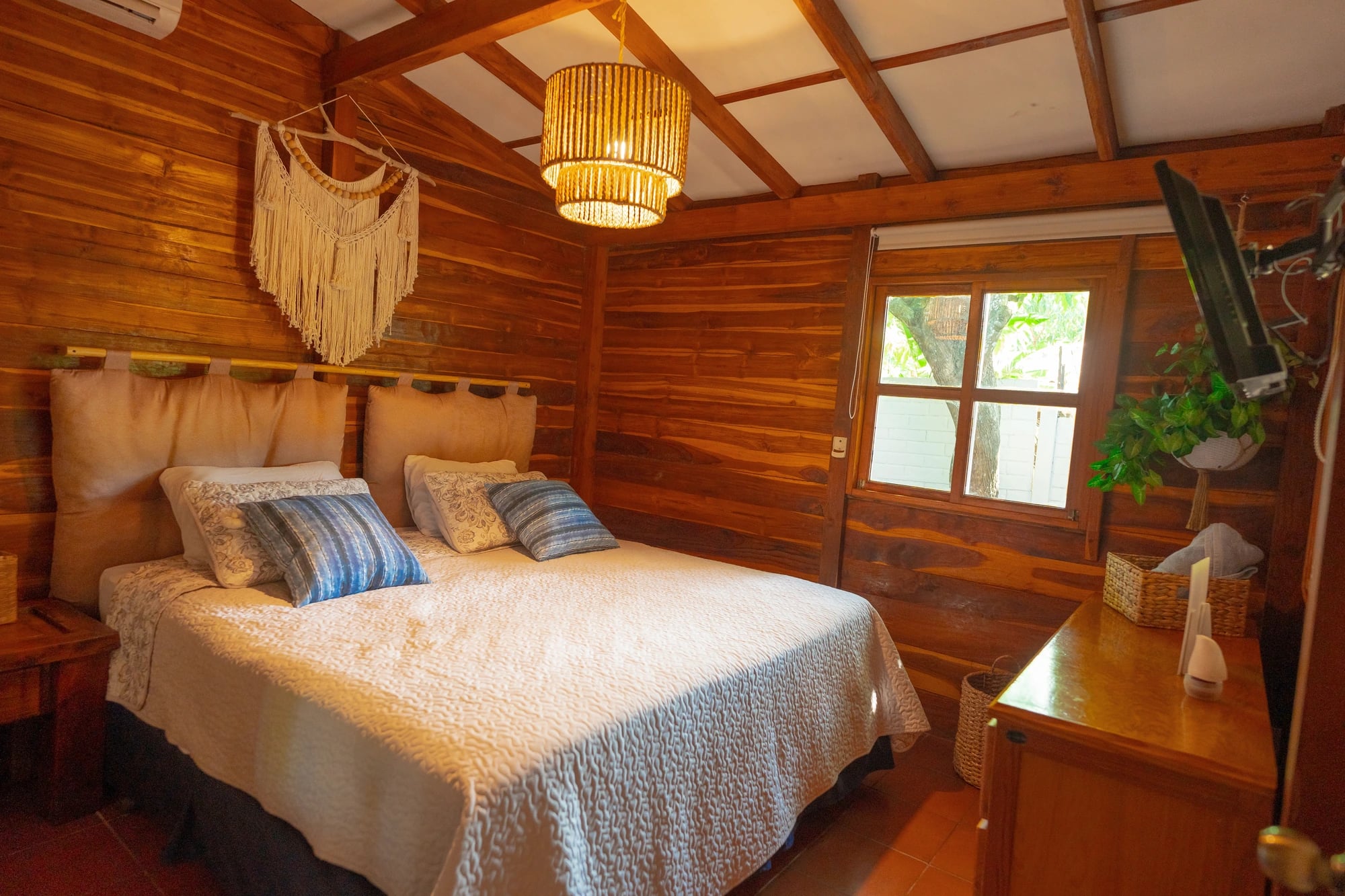 Habitación principal con macramé, lámpara tejida y paredes de madera