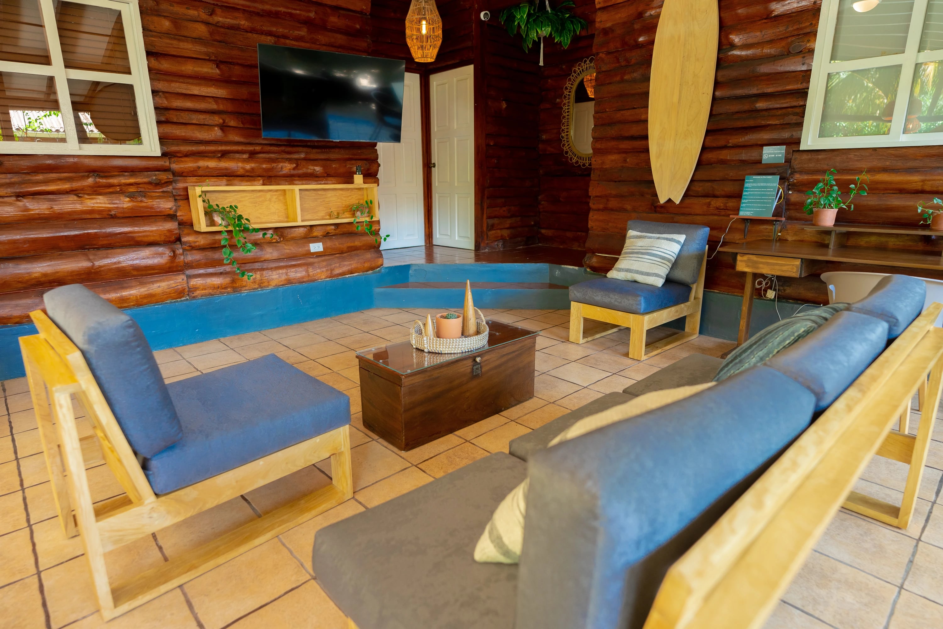 Sala abierta con cojines azules y una tabla de surf en la pared de madera